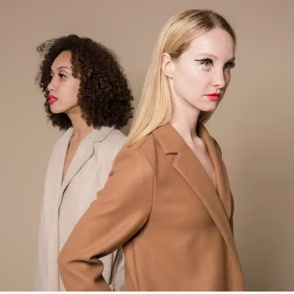 Two women in blazers standing back-to-back in a fashion portrait style.